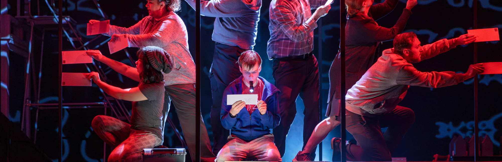 young boy with a flashlight reading a piece of paper surrounded by supporting actors