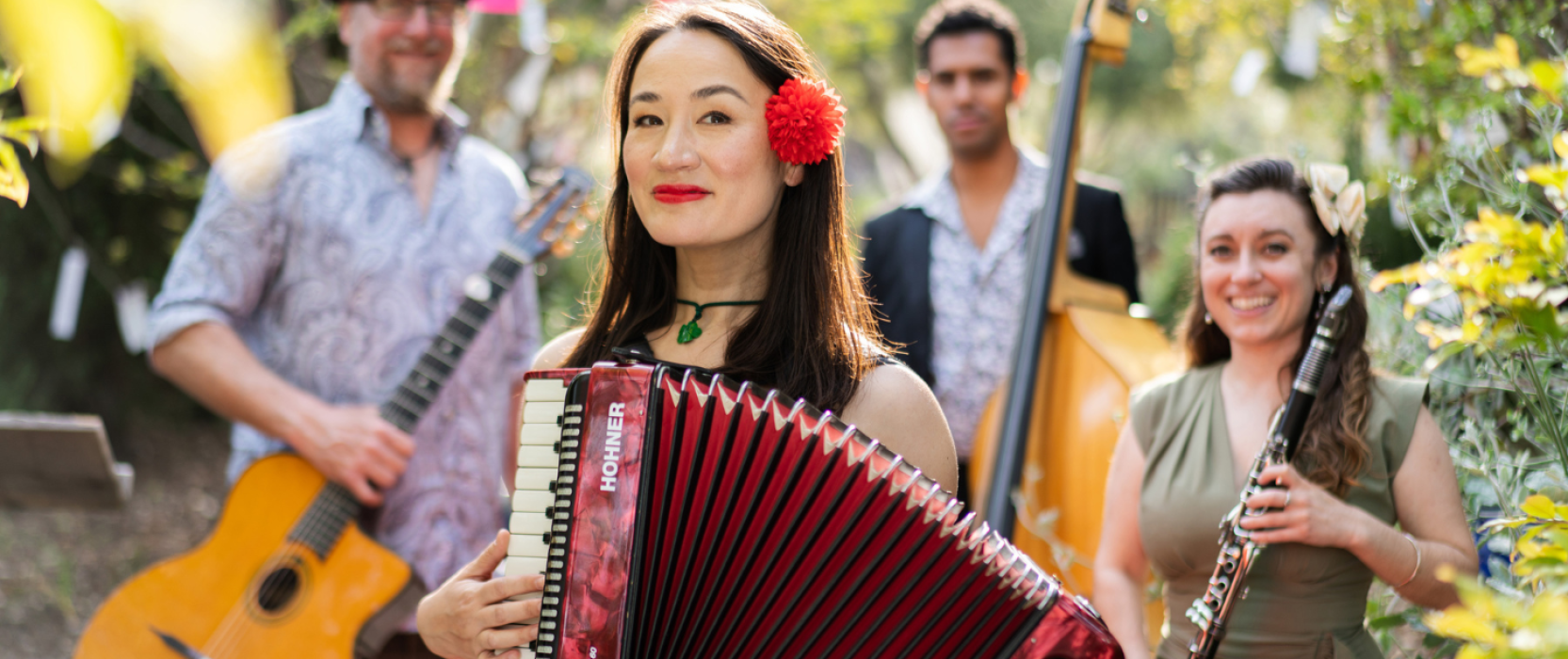 A young woman holding an accordion in the foreground, three band members behind her. 