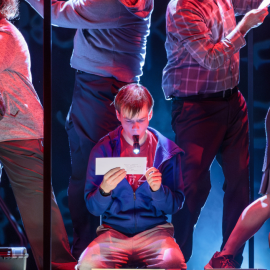 young boy with a flashlight reading a piece of paper surrounded by supporting actors